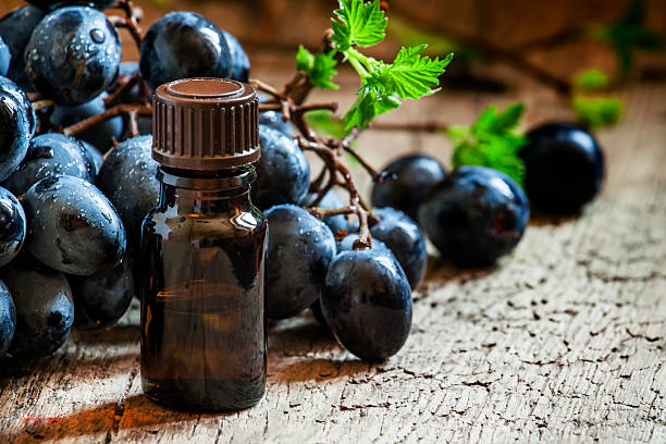 Grape seed oil in brown bottle, bunch of grapes, vine at the old wooden background, selective focus