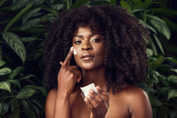 Shot of a beautiful young woman applying moisturiser to her face against a leafy background