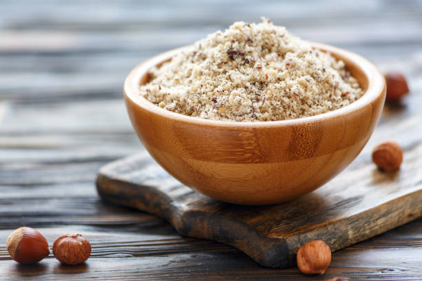 Bowl with hazelnut flour on an old wooden table, selective focus.